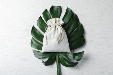 Cotton eco bag  and monstera leaf on white wooden table, top view