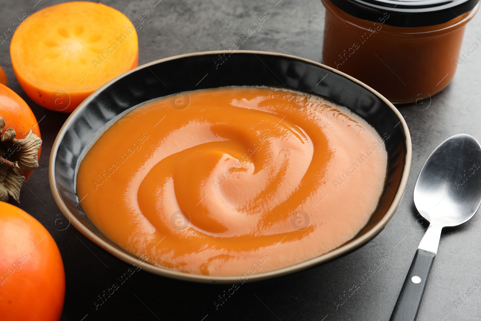 Photo of Delicious persimmon jam in bowl served on gray table, closeup