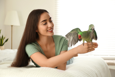 Young woman with Alexandrine parakeet indoors. Cute pet