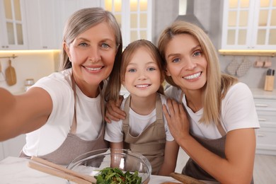 Photo of Three generations. Happy grandmother, her daughter and granddaughter taking selfie in kitchen