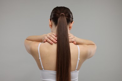 Photo of Woman touching her neck on grey background, back view