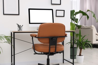 Photo of Comfortable office chair near desk and houseplants in modern workplace