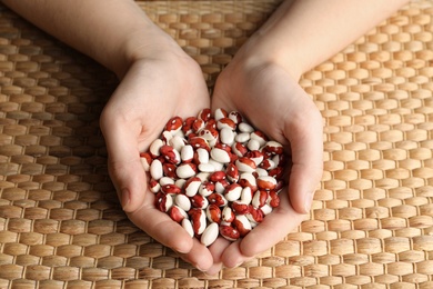 Woman holding pile of beans over wicker table, closeup. Vegetable seeds planting