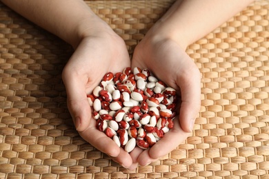 Photo of Woman holding pile of beans over wicker table, closeup. Vegetable seeds planting