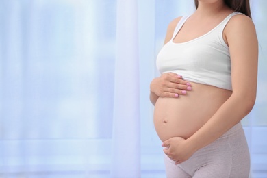 Photo of Young pregnant woman near window at home, closeup