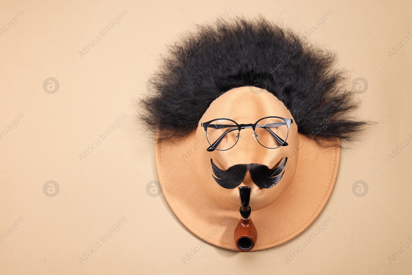 Photo of Man's face made of artificial hair, mustache, glasses and hat on beige background, top view. Space for text