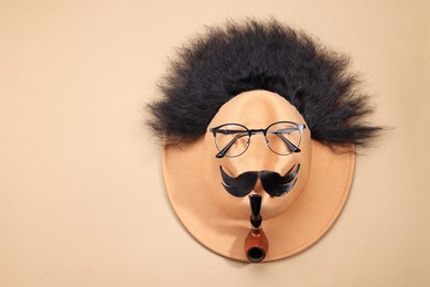 Man's face made of artificial hair, mustache, glasses and hat on beige background, top view. Space for text