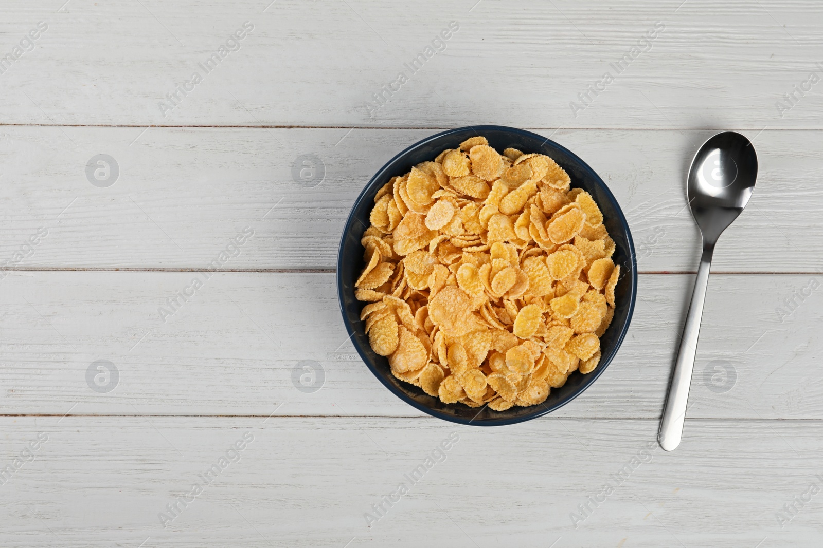 Photo of Bowl with healthy cornflakes and spoon on wooden table, top view. Space for text