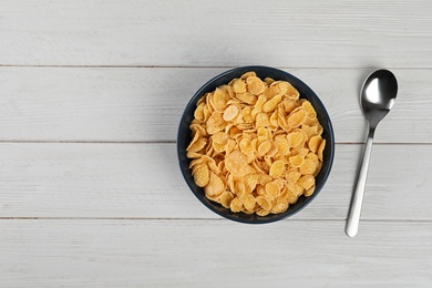 Photo of Bowl with healthy cornflakes and spoon on wooden table, top view. Space for text