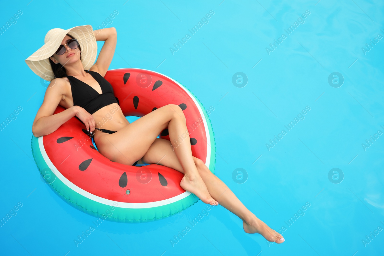 Photo of Young woman wearing stylish black bikini on inflatable ring in swimming pool. Space for text