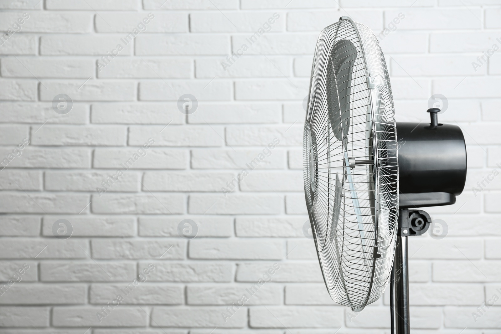 Photo of Electric fan near white brick wall, space for text. Summer heat