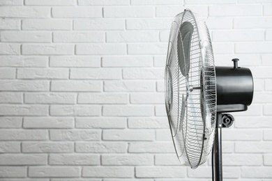 Photo of Electric fan near white brick wall, space for text. Summer heat