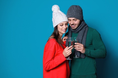 Photo of Young couple in warm clothes clinking glasses of champagne on color background. Christmas celebration