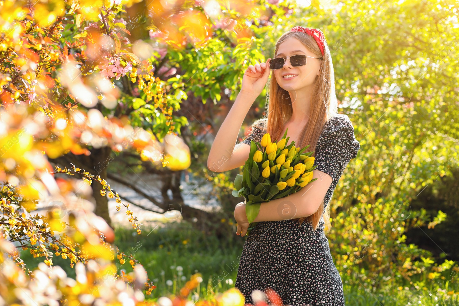 Photo of Beautiful teenage girl with bouquet of yellow tulips in park on sunny day