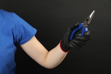 Woman with needle nose pliers on dark background, closeup