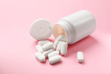 Photo of Bottle and vitamin capsules on pink background