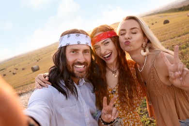 Photo of Happy hippie friends showing peace signs while taking selfie in field