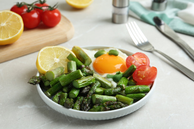 Photo of Oven baked asparagus served with fried egg on light grey marble table