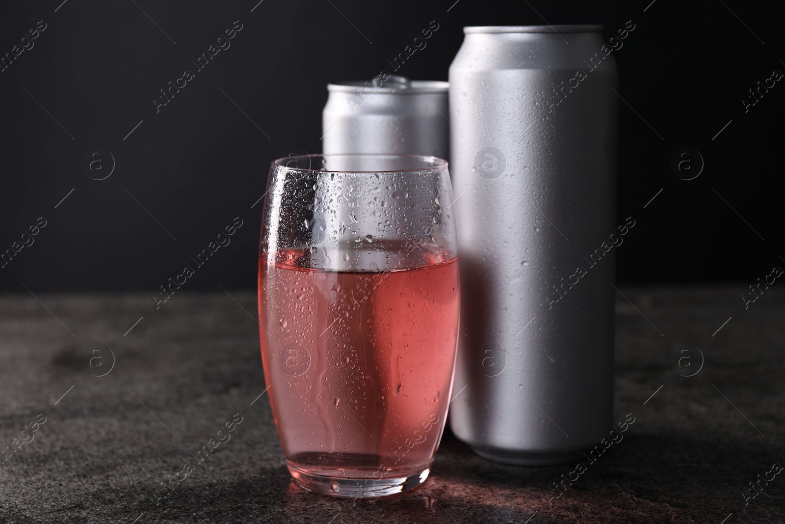 Photo of Energy drink in glass and aluminium cans on grey table, closeup