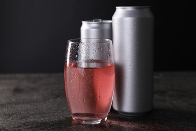 Photo of Energy drink in glass and aluminium cans on grey table, closeup