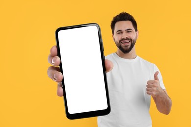 Image of Happy man holding smartphone with empty screen and showing thumbs up on orange background