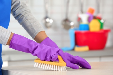 Photo of Woman cleaning table with brush in kitchen, closeup