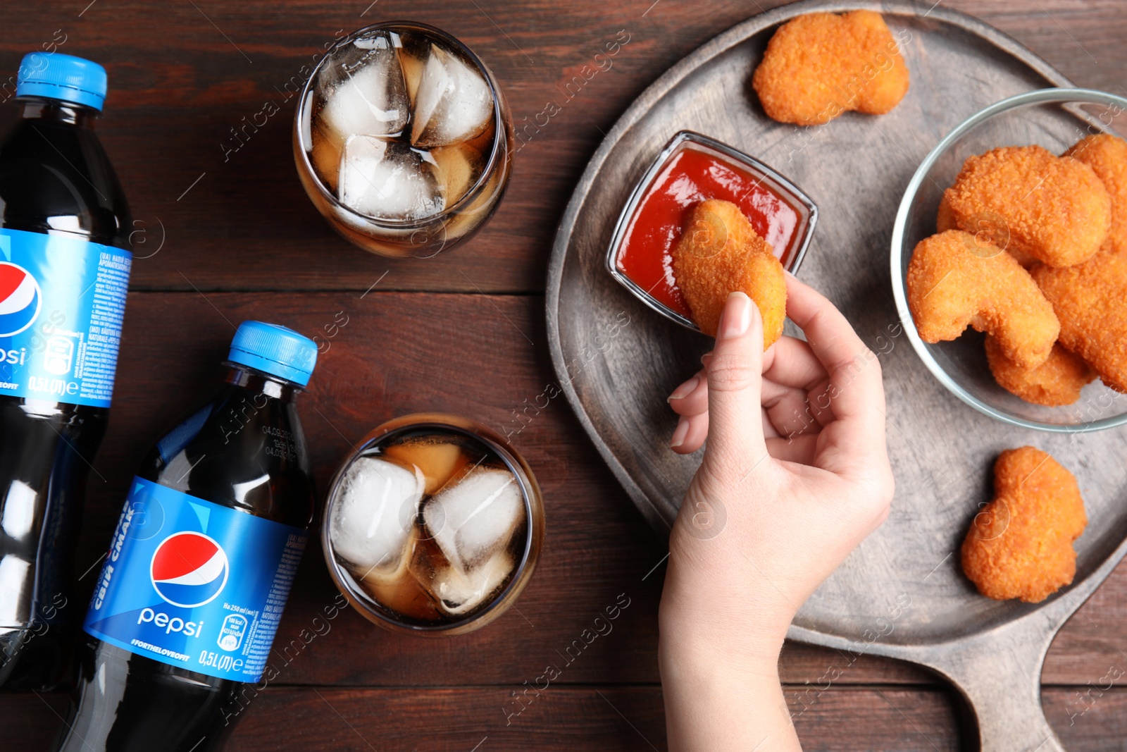 Photo of MYKOLAIV, UKRAINE - FEBRUARY 15, 2021: Woman eating fried chicken at wooden table with glasses and bottles of Pepsi, top view