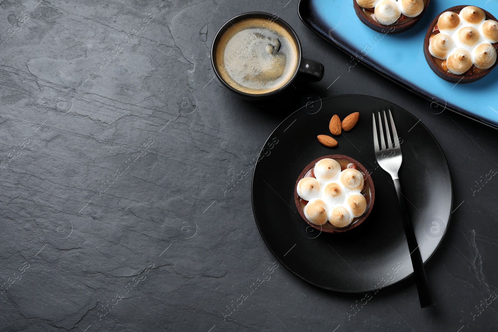 Photo of Delicious salted caramel chocolate tarts with meringue and coffee served on black table, flat lay. Space for text