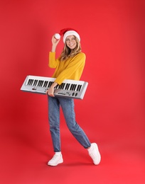 Photo of Young woman in Santa hat with synthesizer on red background. Christmas music