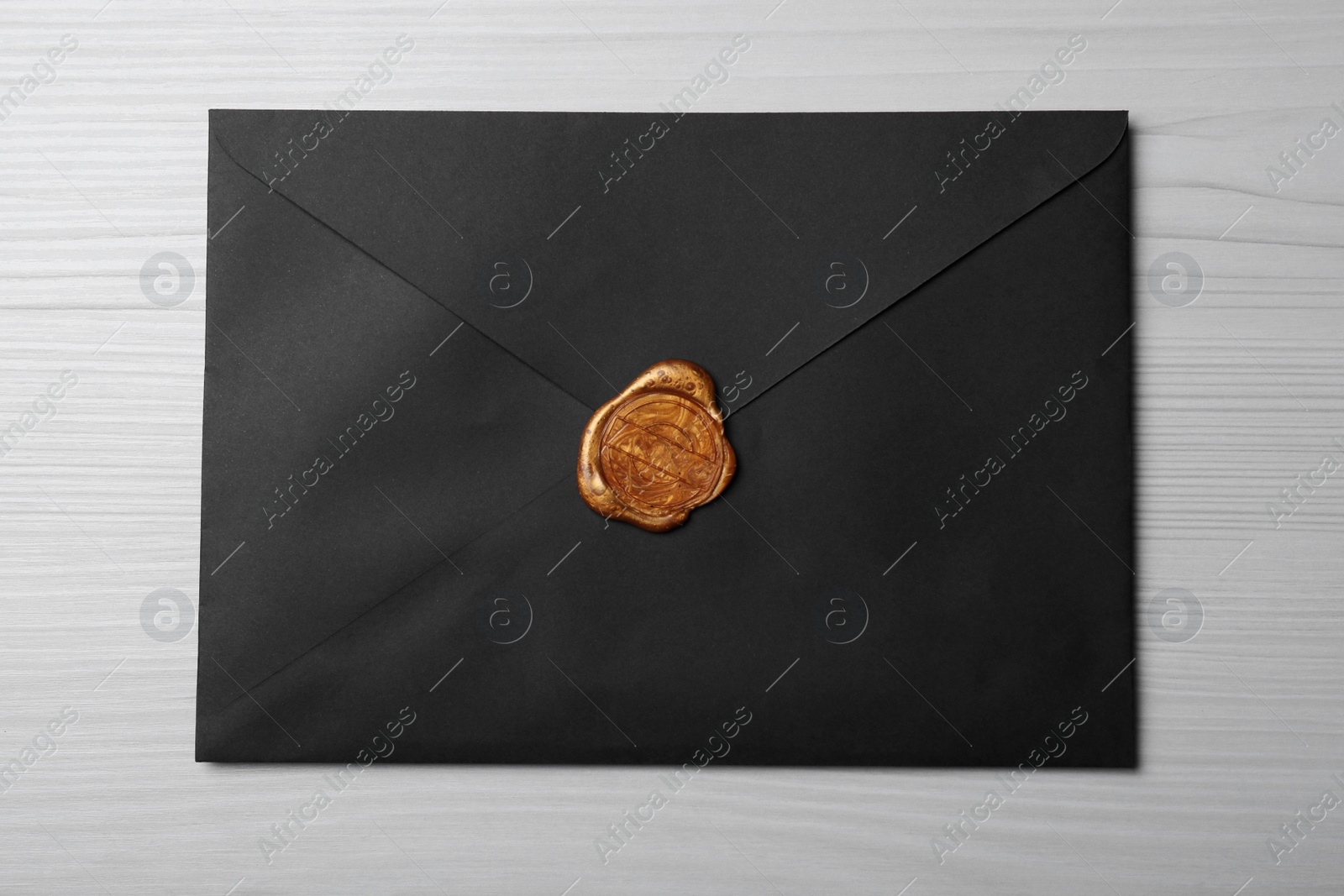 Photo of Black envelope with wax seal on white wooden background, top view