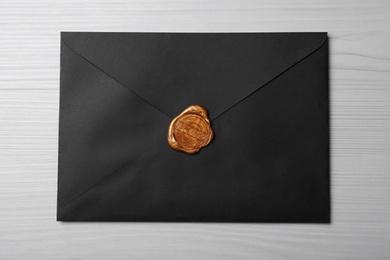 Photo of Black envelope with wax seal on white wooden background, top view