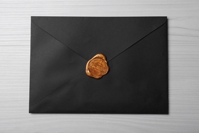 Black envelope with wax seal on white wooden background, top view