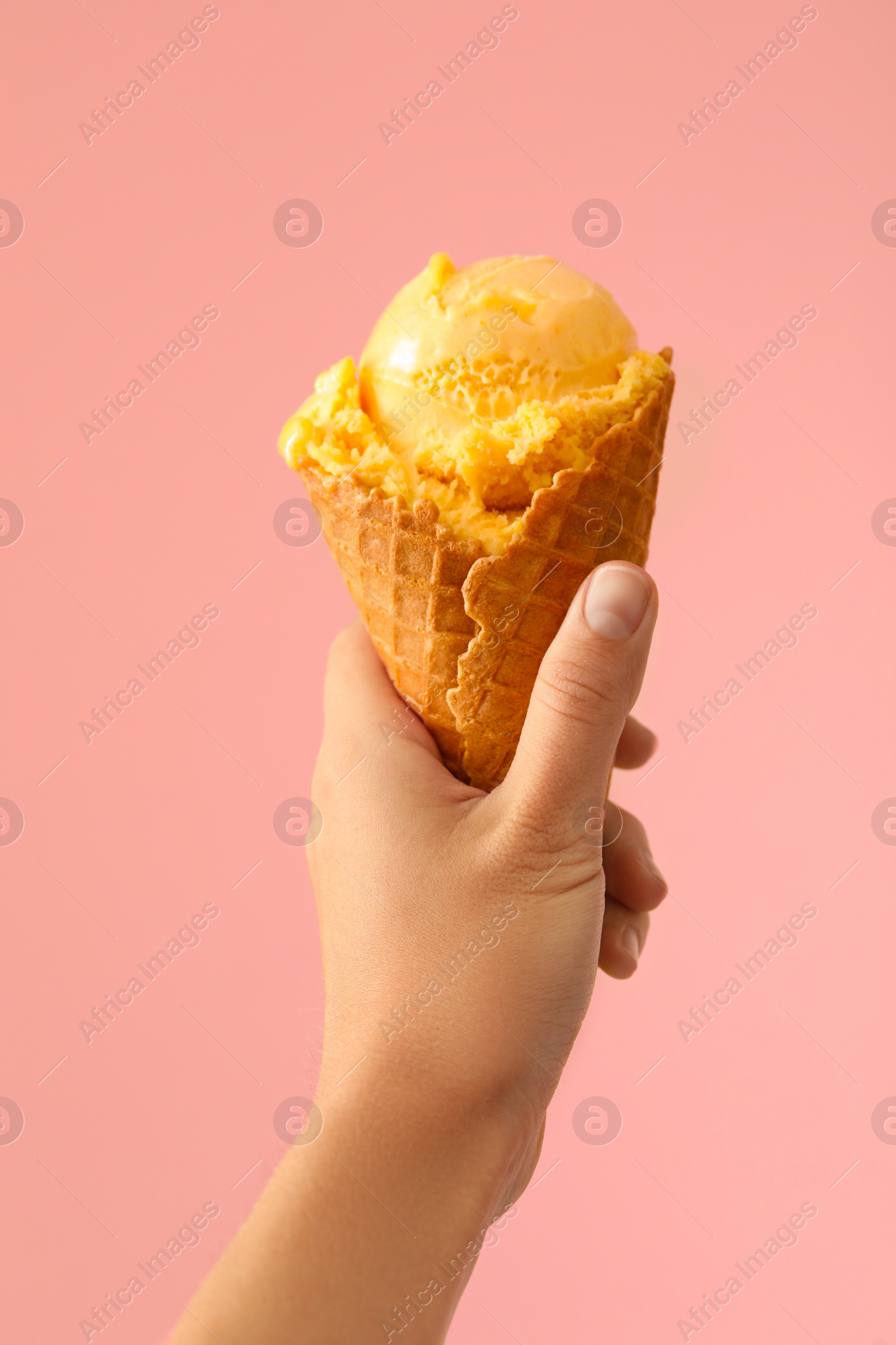 Photo of Woman holding yellow ice cream in wafer cone on pink background, closeup