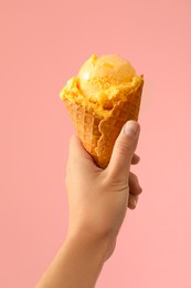 Woman holding yellow ice cream in wafer cone on pink background, closeup