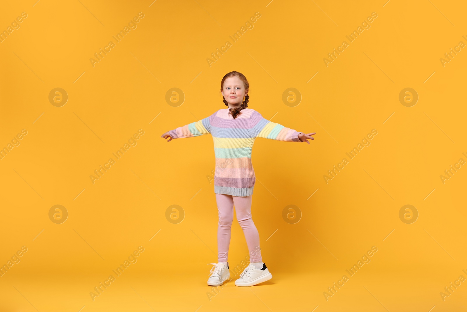 Photo of Cute little girl dancing on orange background