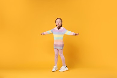 Photo of Cute little girl dancing on orange background