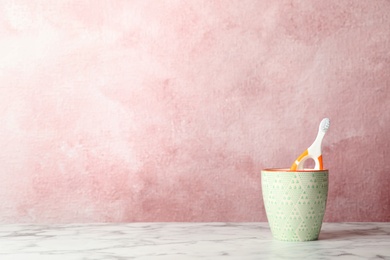 Baby toothbrush in holder on table against color background with space for text