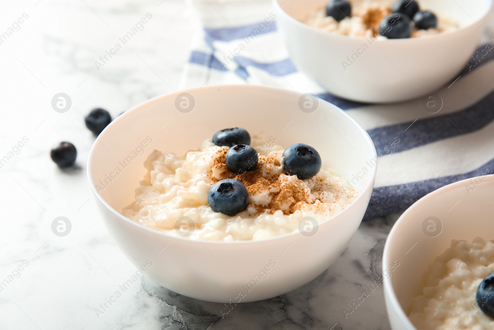 Photo of Creamy rice pudding with cinnamon and blueberries in bowls on marble table