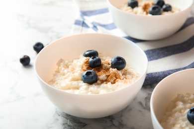 Photo of Creamy rice pudding with cinnamon and blueberries in bowls on marble table