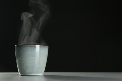 Mug with steam on table against black background. Space for text