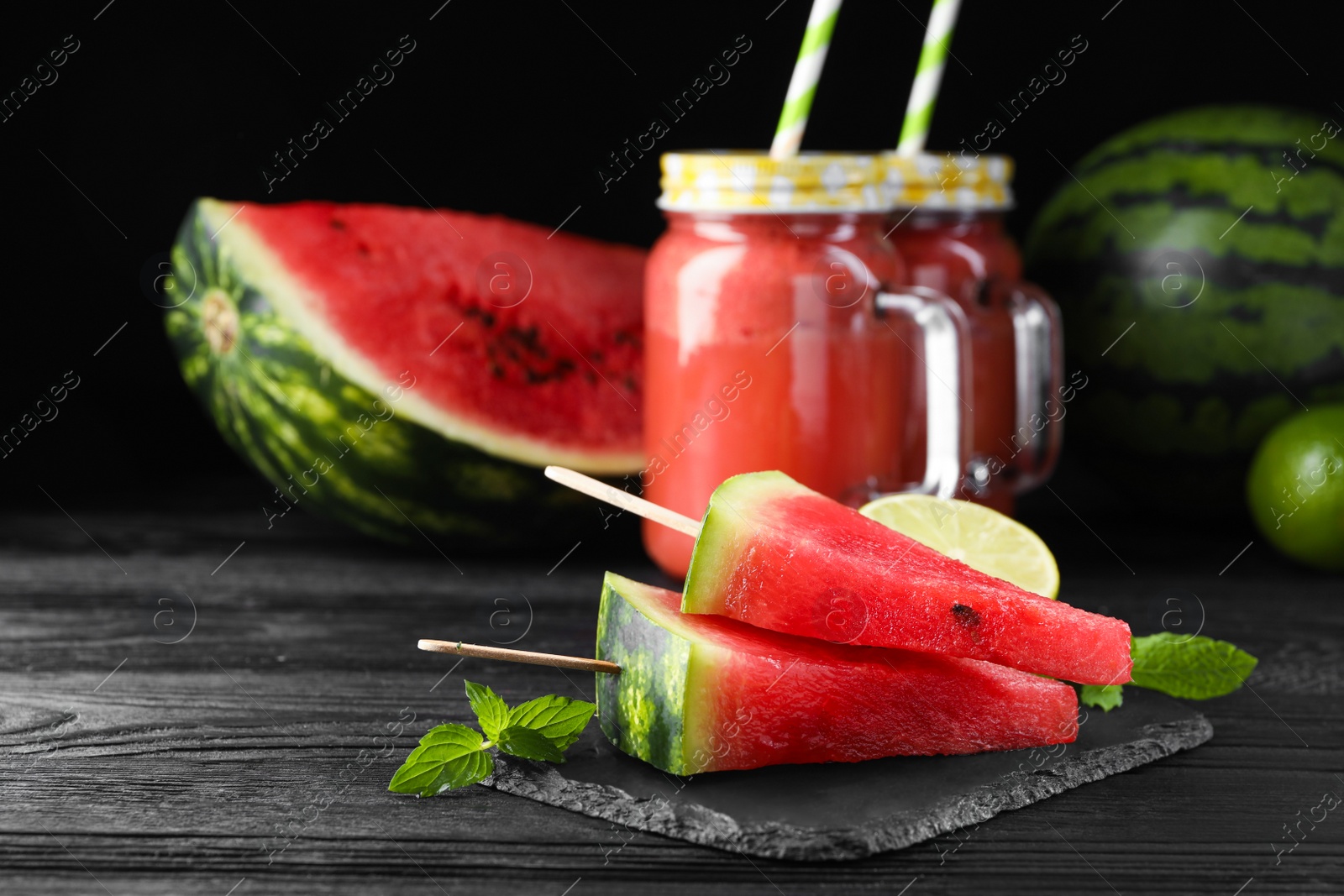 Photo of Slate board with juicy watermelon and lime on black wooden table, space for text