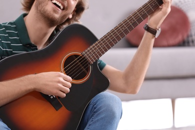 Photo of Young man playing acoustic guitar at home, closeup