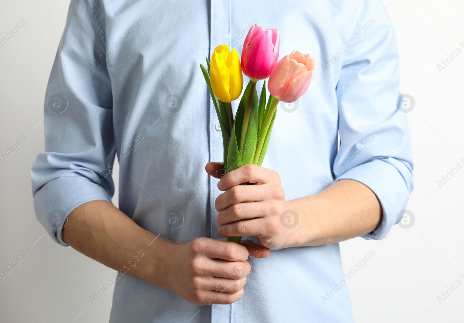 Photo of Man holding beautiful spring tulips on light background, closeup. International Women's Day