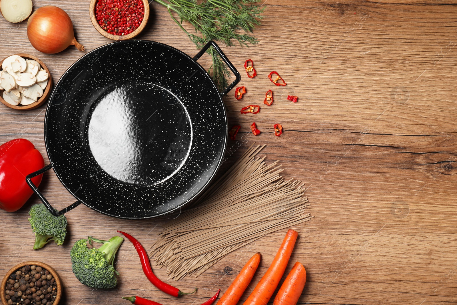 Photo of Empty iron wok surrounded by raw ingredients on wooden table, flat lay. Space for text