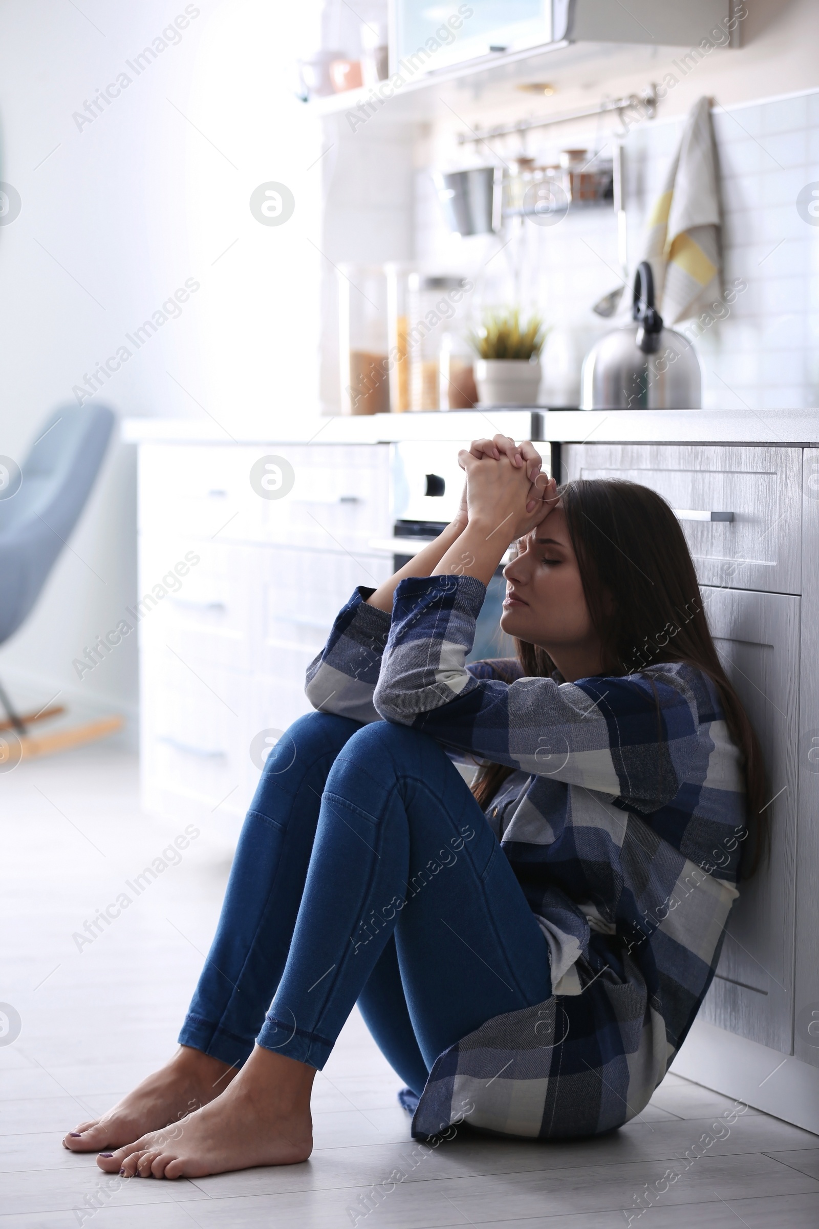 Photo of Depressed young woman sitting on floor in kitchen