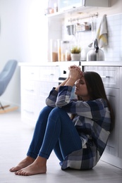 Photo of Depressed young woman sitting on floor in kitchen
