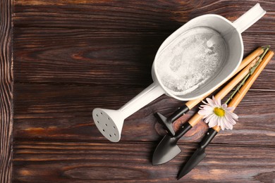 Watering can with gardening tools and flower on wooden table, top view