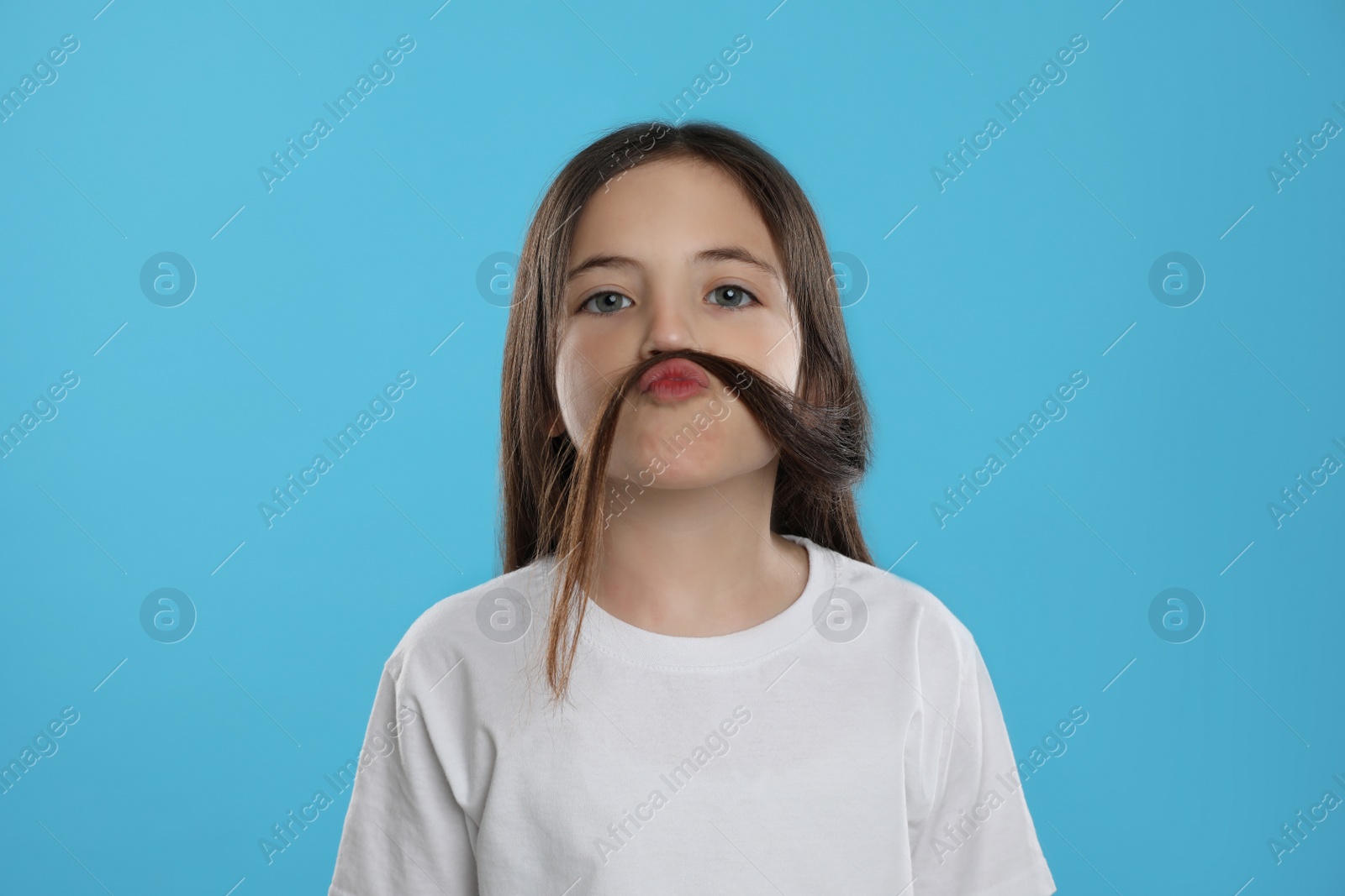 Photo of Cute little girl making fake mustache with her hair on turquoise background