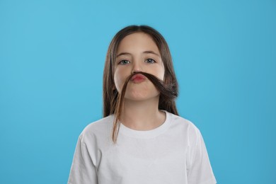 Cute little girl making fake mustache with her hair on turquoise background