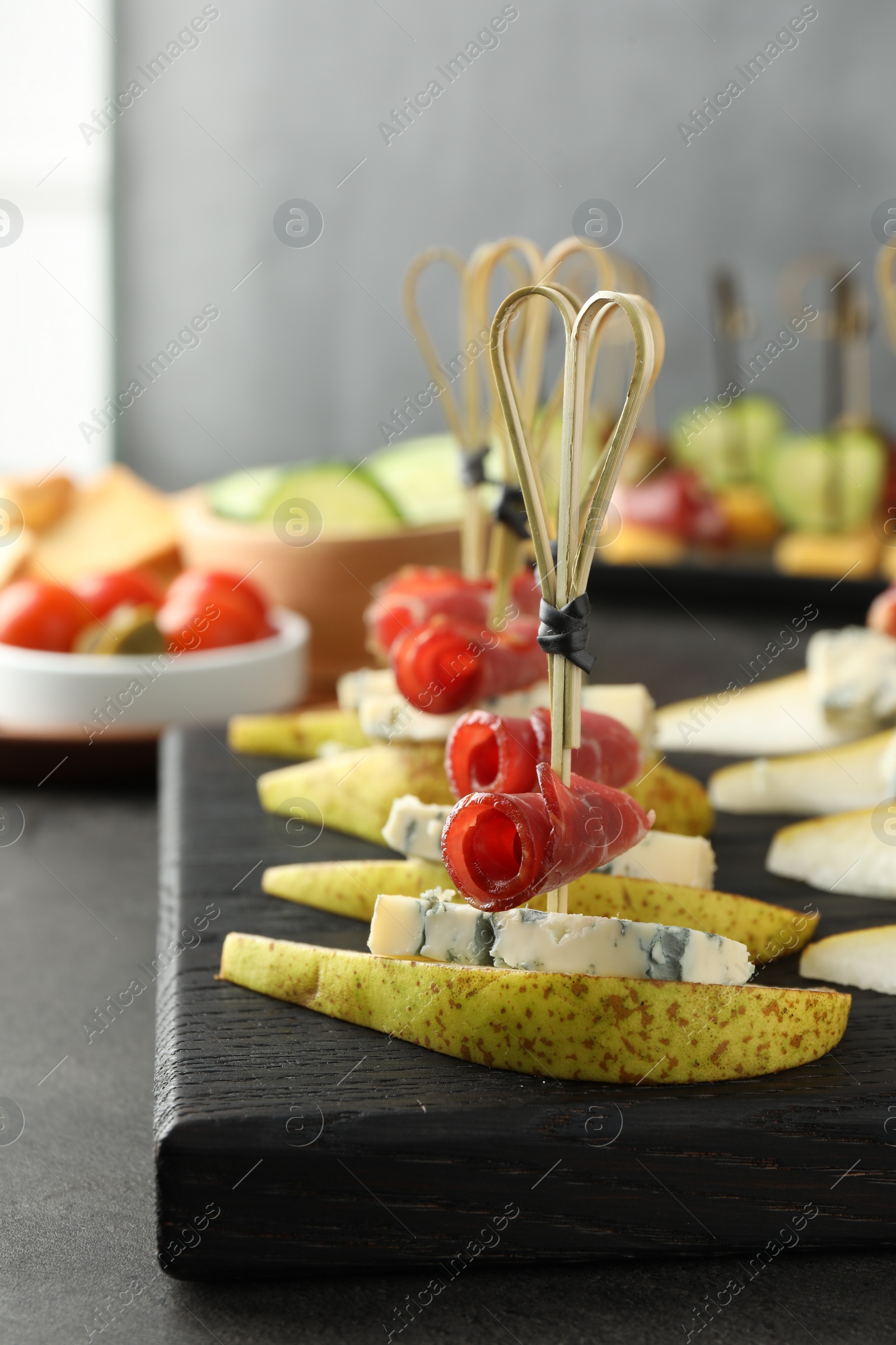 Photo of Tasty canapes with pears, blue cheese and prosciutto on grey table, closeup